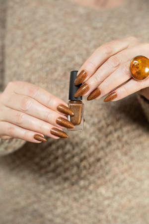 Female hand with long nails and a bottle of golden bronze brown nail polishの写真素材
