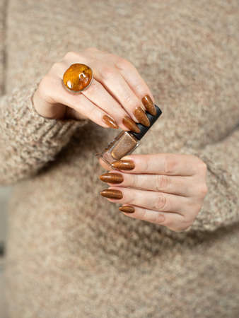 Female hand with long nails and a bottle of golden bronze brown nail polish