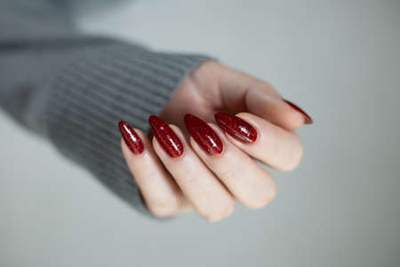 Female hand with long nails and a red manicure holds a bottle of nail polishの写真素材