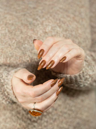 Female hand with long nails and a bottle of golden bronze brown nail polishの写真素材
