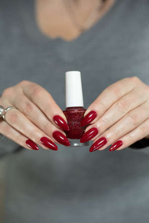 Female hand with long nails and a red manicure holds a bottle of nail polish