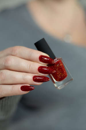 Female hand with long nails and a red manicure holds a bottle of nail polish