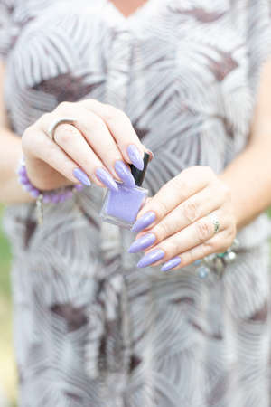 Female hand with long nails and a bottle of blue lilac color nail polish