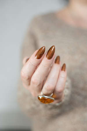 Female hand with long nails and a bottle of golden bronze brown nail polishの写真素材
