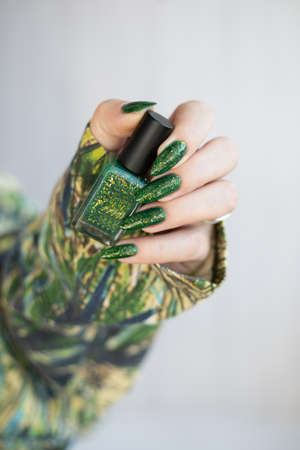 Female hand with long nails and bright green manicure with bottles of nail polishの写真素材