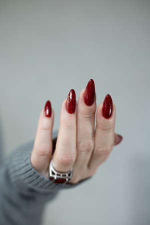 Woman's hands with long nails and a bottle of red orange nail polishの写真素材