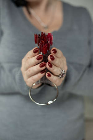 Woman's hands with long nails and a bottle of red orange nail polishの写真素材