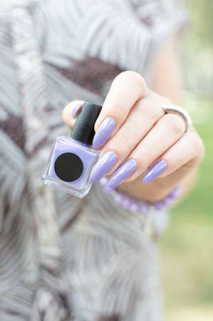 Female hand with long nails and a bottle of blue lilac color nail polish