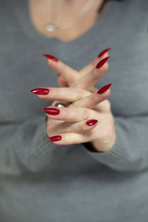 Female hand with long nails and a red manicure holds a bottle of nail polishの写真素材