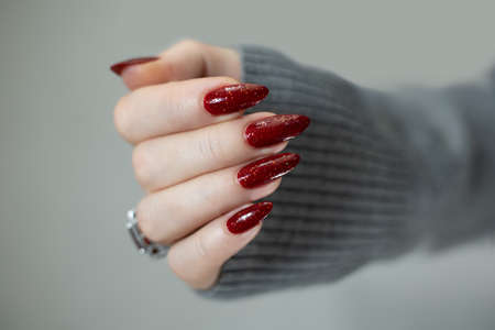 Female hand with long nails and a red manicure holds a bottle of nail polishの写真素材