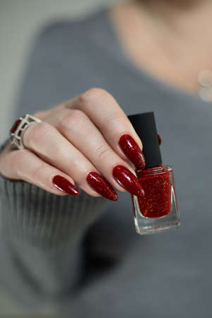 Woman's hands with long nails and a bottle of red orange nail polish