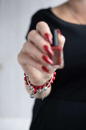 Woman's hands with long nails and a bottle of red orange nail polishの写真素材