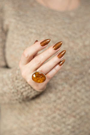 Female hand with long nails and a bottle of golden bronze brown nail polishの写真素材