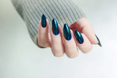 Woman's beautiful hand with long nails and turquoise green and blue manicure with bottles of nail polishの写真素材
