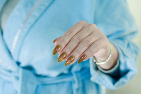 Female hand with long nails and a bottle of golden yellow mustard nail polish