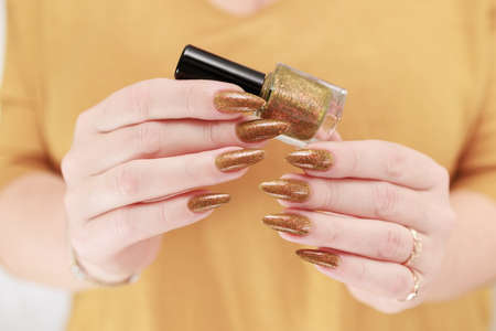 Female hand with long nails and a bottle of golden yellow mustard nail polishの写真素材