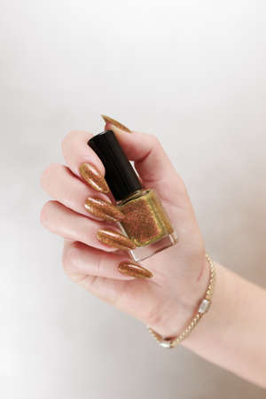 Female hand with long nails and a bottle of golden yellow mustard nail polishの写真素材