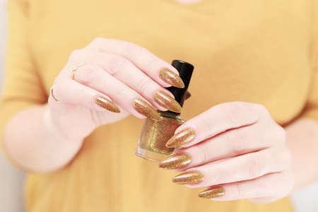 Female hand with long nails and a bottle of golden yellow mustard nail polishの写真素材