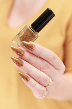 Female hand with long nails and a bottle of golden yellow mustard nail polish
