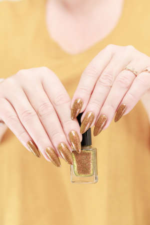 Female hand with long nails and a bottle of golden yellow mustard nail polishの写真素材