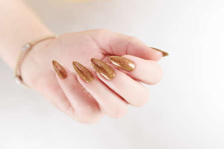 Female hand with long nails and a bottle of golden yellow mustard nail polish