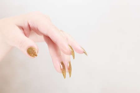 Female hand with long nails and a bottle of golden yellow mustard nail polishの写真素材