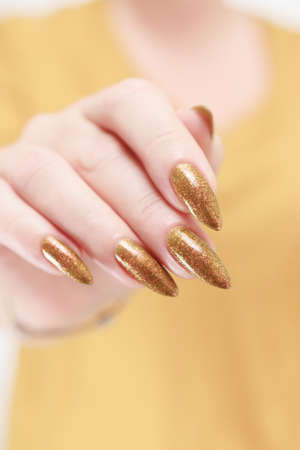 Female hand with long nails and a bottle of golden yellow mustard nail polishの写真素材