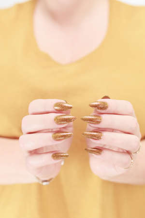 Female hand with long nails and a bottle of golden yellow mustard nail polishの写真素材