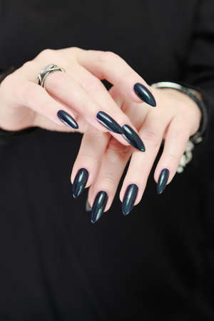 Female hand with long nails and dark purple blue manicure holds a bottle of nail polishの写真素材