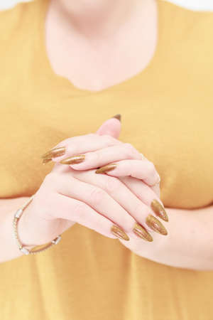 Female hand with long nails and a bottle of golden yellow mustard nail polishの写真素材