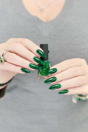 Woman's hand with long nails and green manicure with bottles of nail polish