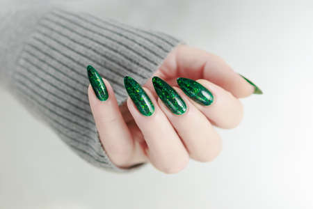 Woman's hand with long nails and green manicure with bottles of nail polishの写真素材