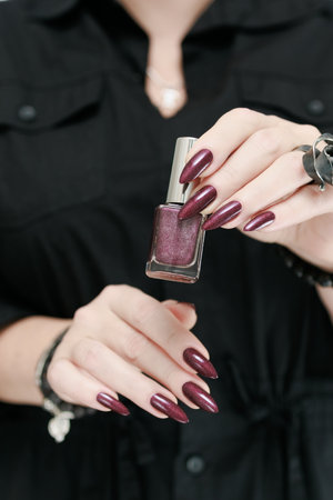 Woman's hands with long nails and a bottle of dark red bordo nail polish