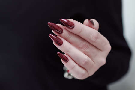 Woman's hands with long nails and a bottle of dark red bordo nail polish