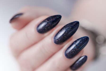 Woman's hands with long nails and black manicure with bottles of nail polishの写真素材