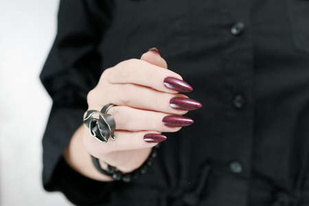 Woman's hands with long nails and a bottle of dark red bordo nail polishの写真素材