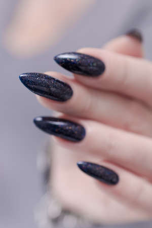 Female hand with long nails and black manicure holds a bottle of nail polish