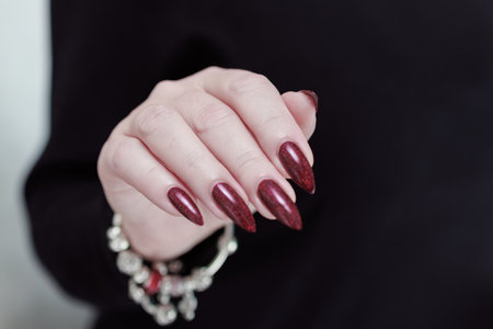 Woman's hands with long nails and a bottle of dark red bordo nail polishの写真素材