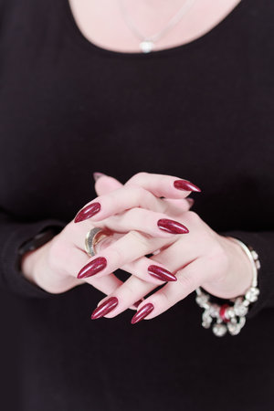 Woman's hands with long nails and a bottle of dark red bordo nail polishの写真素材