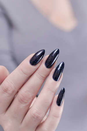 Female hand with long nails and black manicure holds a bottle of nail polishの写真素材