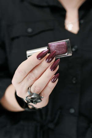 Woman's hands with long nails and a bottle of dark red bordo nail polish
