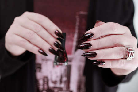 Woman's hand hand with long nails and black manicure with bottles of nail polish