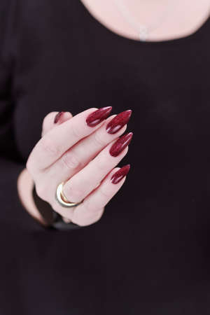 Woman hand with long nails and a bottle of dark red burgundy nail polishの写真素材