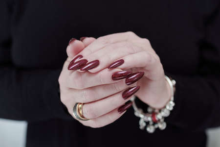 Woman hand with long nails and a bottle of dark red burgundy nail polishの写真素材