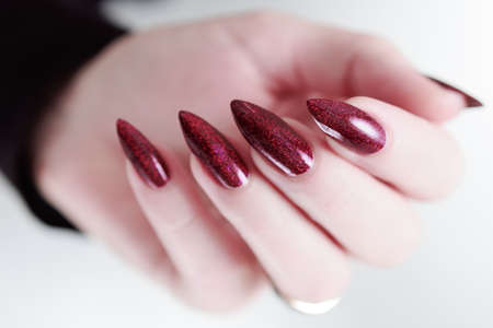 Woman hand with long nails and a bottle of dark red burgundy nail polishの写真素材