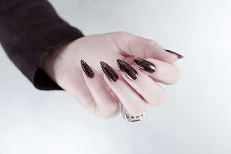 Woman's hand hand with long nails and black manicure with bottles of nail polishの写真素材