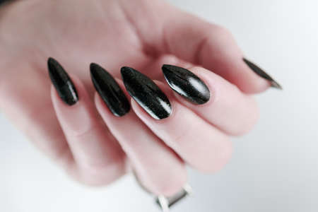 Female hand with long nails and black manicure holds a bottle of nail polishの写真素材