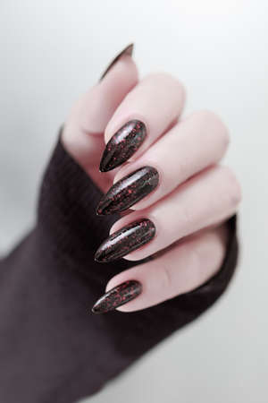 Female hand with long nails and black manicure holds a bottle of nail polish