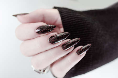 Female hands with long nails and black and red manicure holding a bottle of nail polishの写真素材