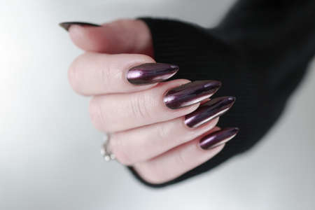 Female hand with long nails and dark purple manicure holds a bottle of nail polishの写真素材